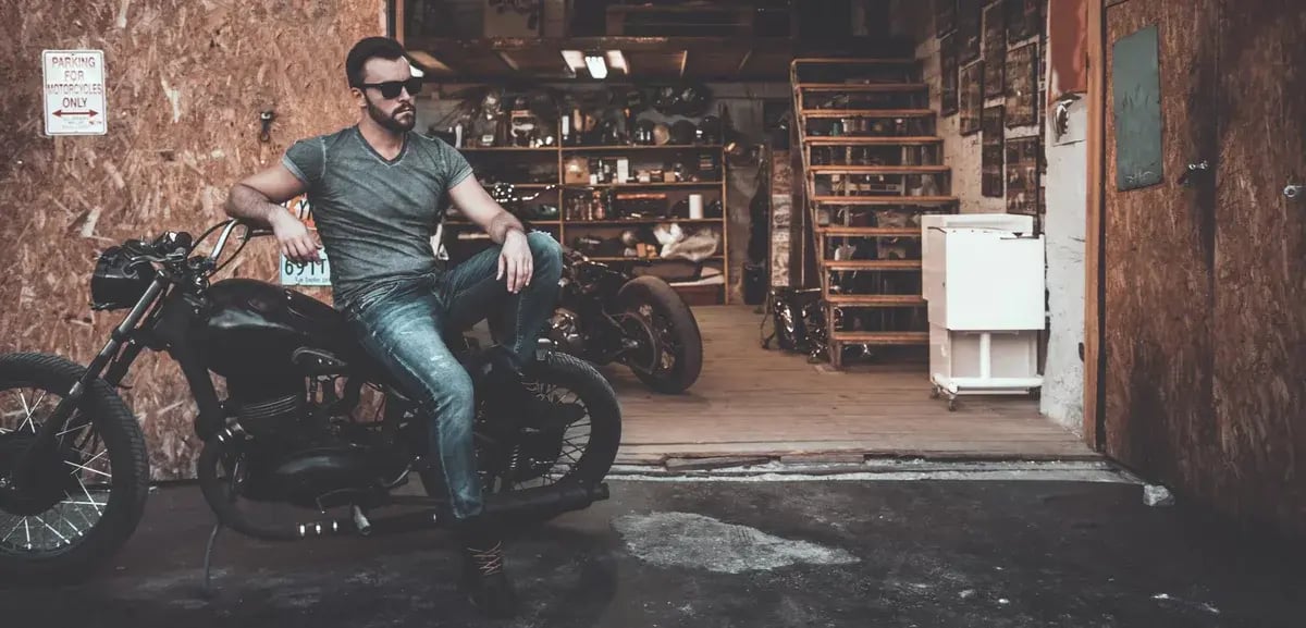A man sitting on his motorcycle in a shop.