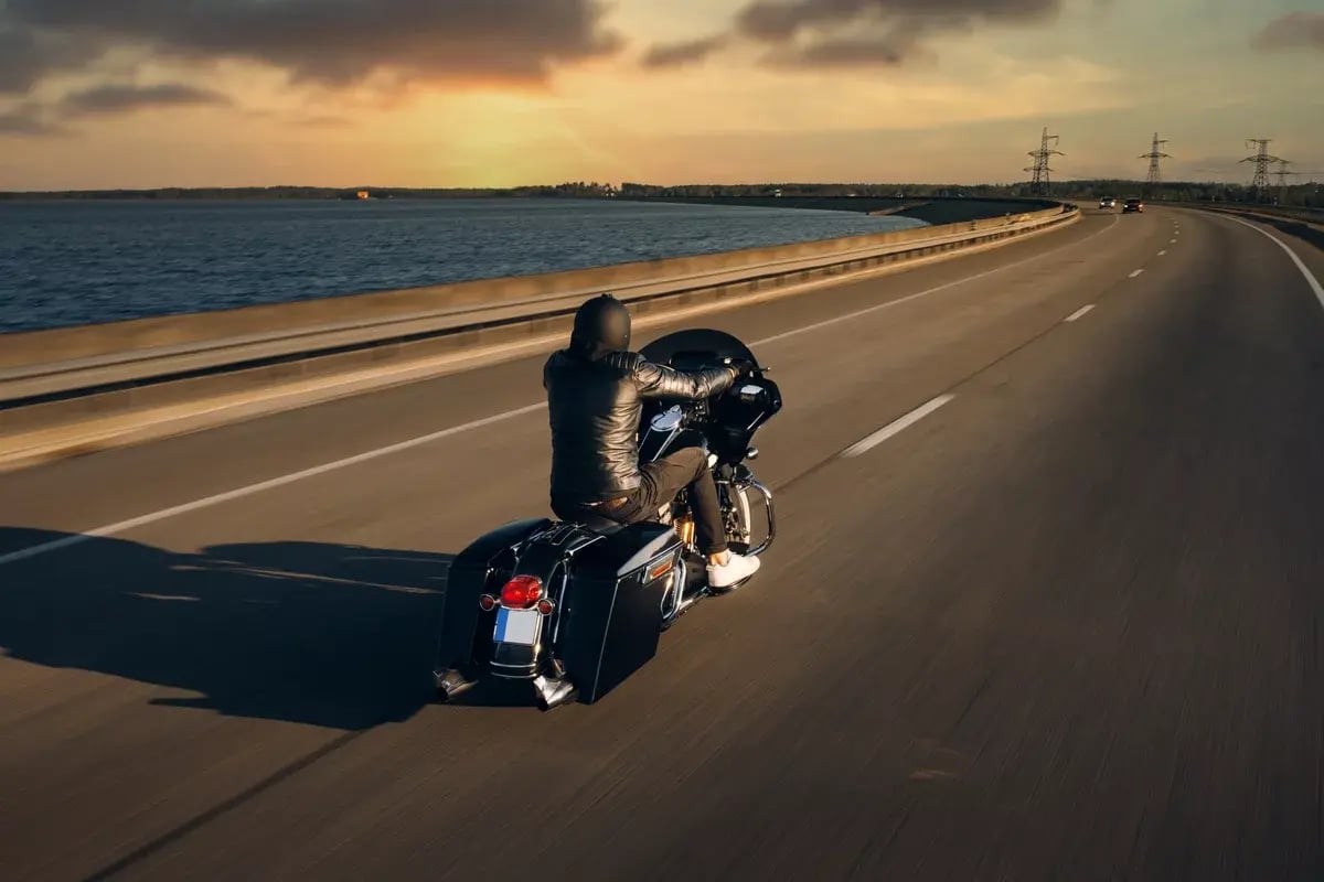 A motorcycle driver rides alone on an asphalt highway.