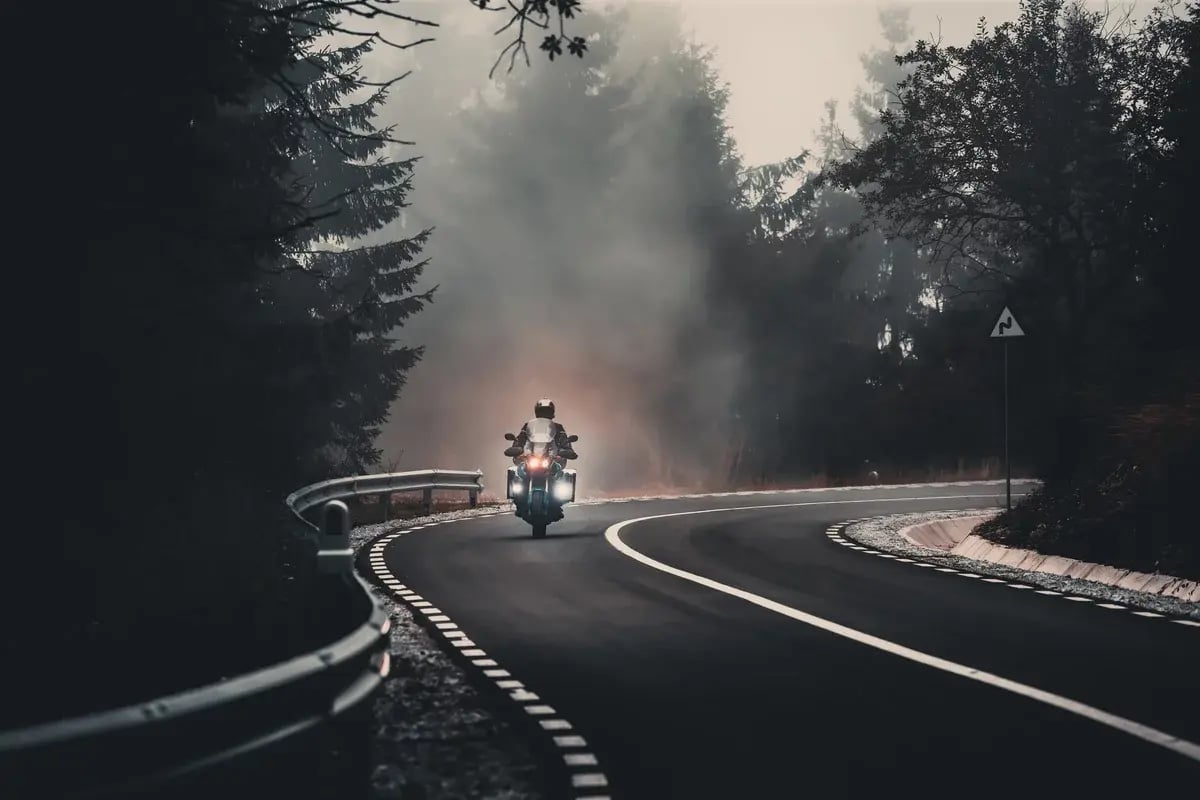 A motorcycle on a foggy, forested road.