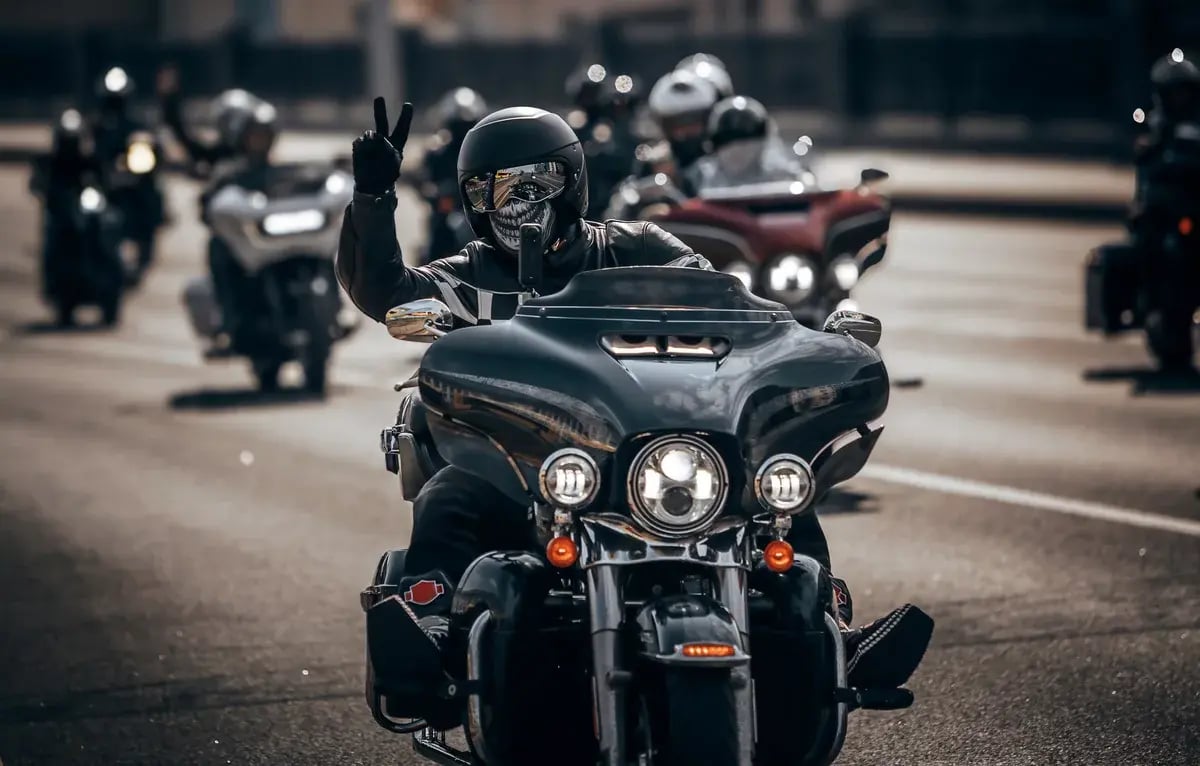 A biker dressed in black gear and a skull mask rides in a motorcycle column through the city, creating a bold and striking image
