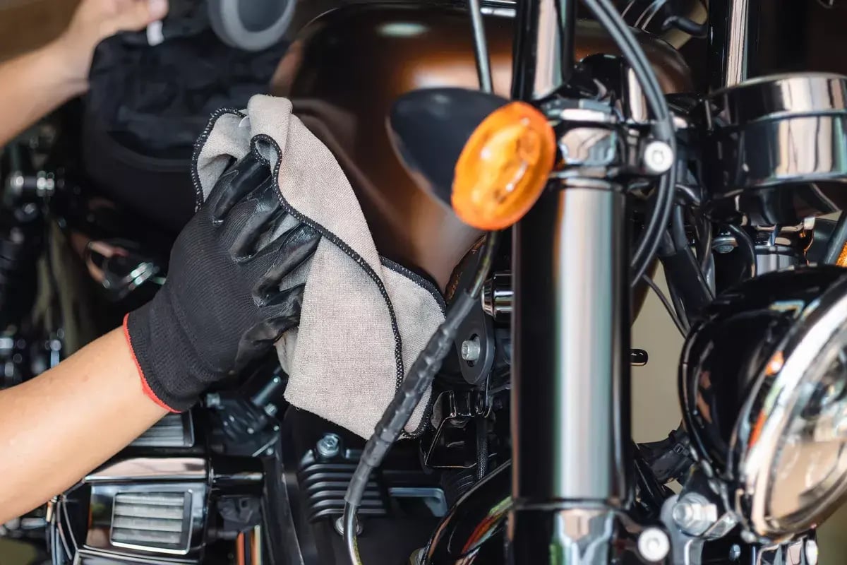 Maintenance worker wiping a motorcycle fuel tank.
