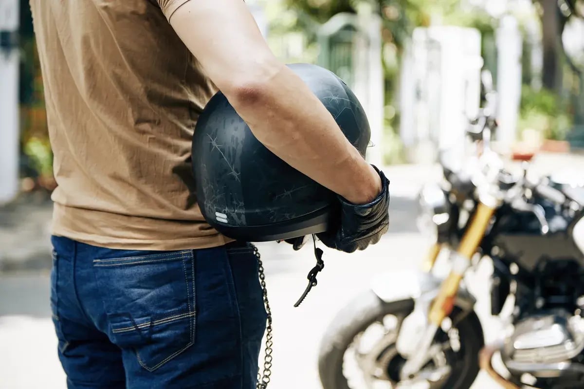 Man with helmet in hands looking at his motorcycle, selective focus