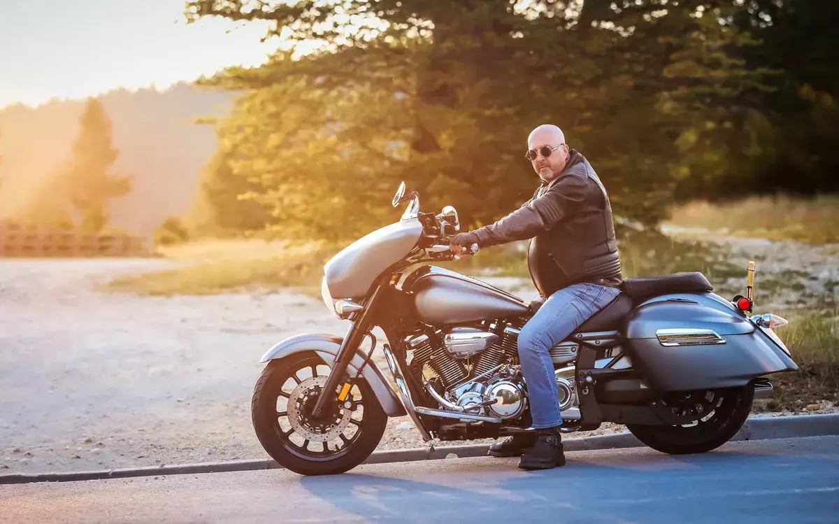 Stylish middle-aged man in a leather jacket sits confidently on a large cruiser motorcycle at sunset.