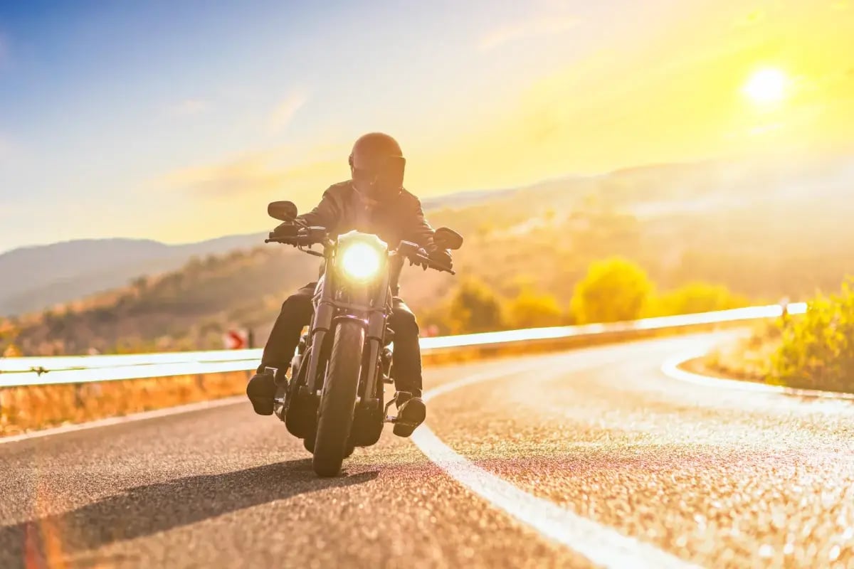 Sunset over an open road and a man with a helmet riding a chopper
